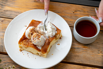 A warm slice of cake topped with cream and nuts sits on a plate alongside a steaming cup of coffee. This delightful combination is ideal for an afternoon snack, offering a sweet moment of joy
