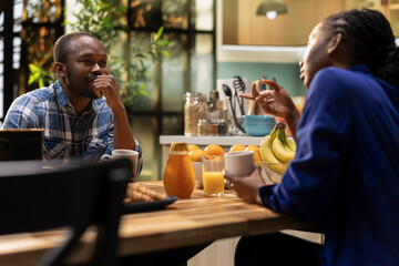 African american lovers chatting over their coffee at the breakfast table, enjoying free weekend morning at home and relaxing together. Young man and woman enjoy a chill lifestyle.
