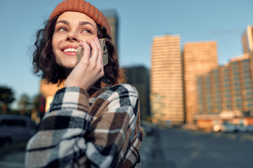 Woman phone smile city beanie coat golden hour: candid lifestyle portrait of a smiling young woman...