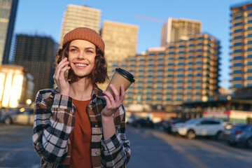 woman with coffee and phone in urban street, smile and candid beanie portrait at golden hour,...