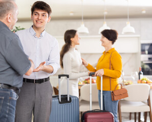 Young couple warmly greeting parents returning home from trip. Hospitable friendly young guy shaking hand with father-in-law in cozy family atmosphere