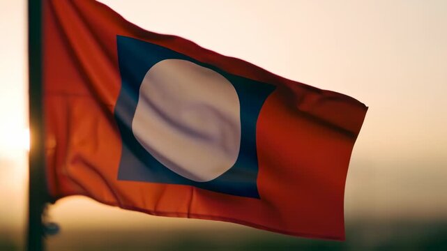 A vibrant flag flutters in the gentle breeze, displaying a bold blue shape at its center against a bright orange background. The sun sets in the distance, casting warm tones across