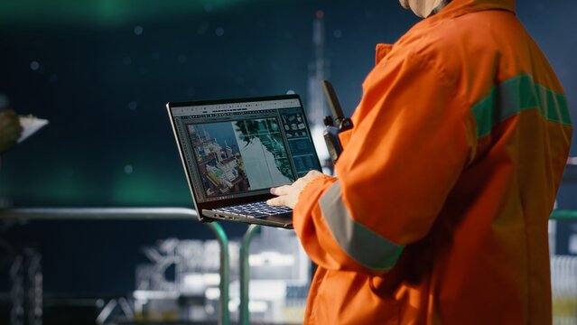 Male engineer on offshore drilling rig inspecting emission systems under aurora borealis, ensuring compliance and responsible petroleum extraction in marine environments.