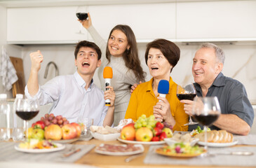 Laughing happy family singing together, parents and adult children having party singing song using microphone at home