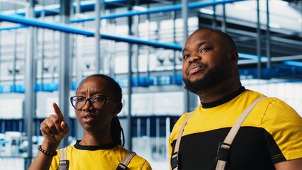 Smart factory coworkers talking, working together to test automated systems. Industry 4.0 industrial plant teamworking colleagues identify bottlenecks and optimize gear based on data, camera A