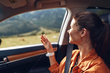 Naklejka premium Woman seated in a car, gazing out the window at a scenic landscape, enjoying a peaceful travel moment under bright daytime light in a moving road setting.
