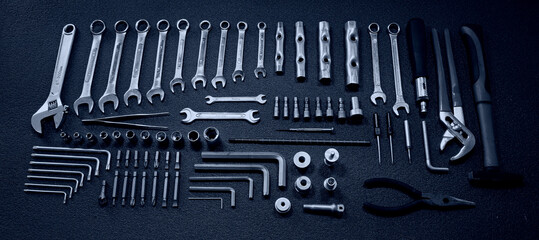 Fototapeta premium Flat lay stock photo of big set of mechanical tools, spanners, hex wrenches and socket bits on a clean black surface of work table in blue back lit 