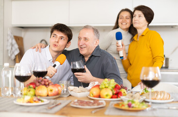 Party and karaoke at house for fun social event or gathering together in celebration. Happy family singing song using microphone at festive table at home