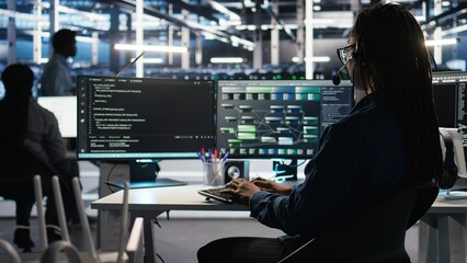 Data center employee uses audio headset and visual programming dashboard to troubleshoot client reported issues. Server farm technician looks at node tree interface, talking in microphone