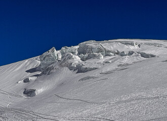 Rocky alpine ridge surrounded by fresh winter snow under a clear deep blue sky. High-altitude landscape of the Swiss Alps with dramatic textures and untouched terrain.