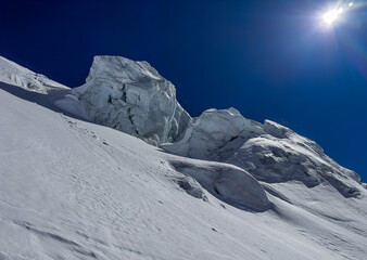 Snowy Alpine ridge with sharp ice formations under a deep blue sky in bright winter sunlight. High-altitutde landscape showcasing rugged textures and prisitine mountain scenery.
