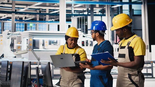 Engineering group in solar panel factory adjusting machinery settings through tablet, inspecting the production and configuration for efficient production. Teamworking. Camera B.