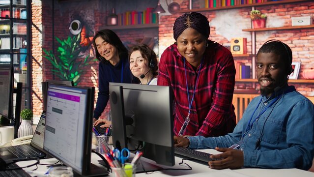 Smiling multiethnic technical support team in diverse call center office doing troubleshooting. Cheerful multiracial IT staff members fixing customer connectivity issues, camera B - Powered by Adobe