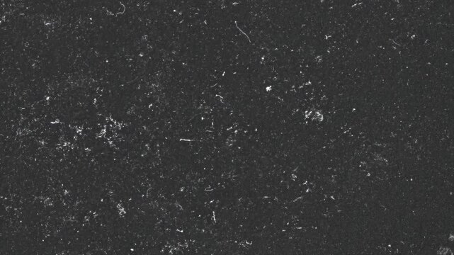 A textured black surface with speckles and subtle imperfections, resembling a material or background.