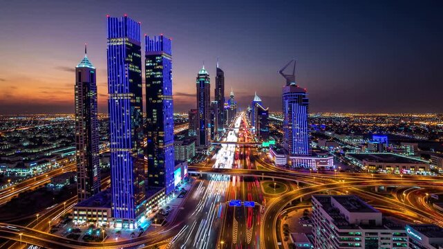 Tall skyscrapers adorned with vibrant lights stand proudly against a twilight sky, illuminating the bustling city below. The busy highways weave through the urban landscape, showca