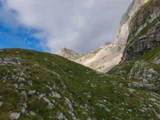 Epic alpine mountains landscape of the Mangart massive rugged cliffs with atmospheric light from the cloudy sky 