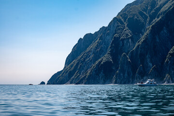 Serene coastal landscape with majestic cliffs, calm blue ocean, and distant boat on a clear day showing the tranquil beauty of nature and sea adventures