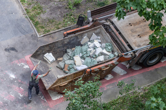Overhead view of male worker managing construction waste disposal, caucasian, mature, in a large metallic dumpster filled with debris bags and building materials