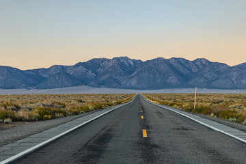 Iconic straight stretch of Freeway at sunset, leading directly toward dramatic eastern escarpment of the Sierra Nevada across the vast high-desert plain near Hot Creek, California.