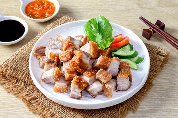 Crispy pork belly on white plate and dipping sauce on the wooden table