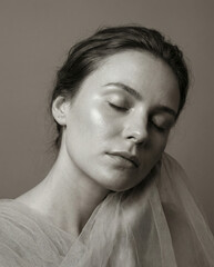 Minimalist conceptual beauty portrait of a woman with closed eyes and sheer tulle fabric draped over her shoulder, black and white fine art