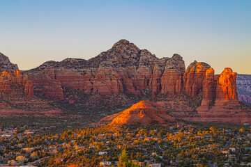 Majestic red sandstone formations tower above the town of Sedona at dusk. The soft evening light highlights the rugged cliffs and desert terrain of northern Arizona.