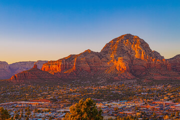 A warm golden-hour view of Sedona, Arizona, with dramatic red rock formations glowing under sunset...
