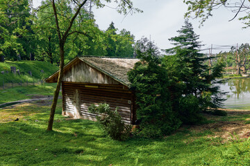 Naklejka premium Cabin boathouse lake trees grass forest scene with rustic wooden structure by water, peaceful countryside landscape, summer greenery, sunlight and reflections on the shore.
