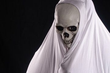 Spooky Grim Reaper wearing white hooded cloak with skeleton skull face. Creepy ghost or specter portrait looking down on black background for Halloween horror concept.