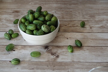 Fresh cucamelons in white bowl on rustic wood table