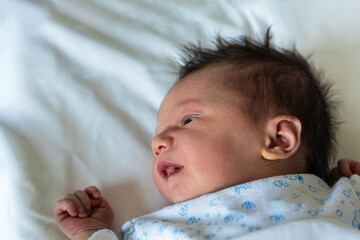 Newborn baby waking up on a white bed close-up