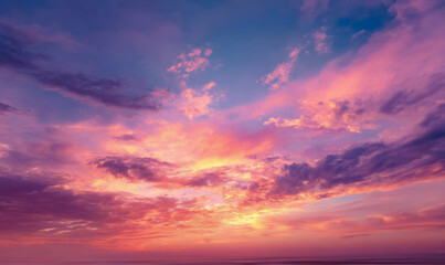 Obraz premium Bright clouds in vivid tones stretch across the sky at sunset, casting reflections on the ocean surface. The dramatic light creates a striking natural scene.