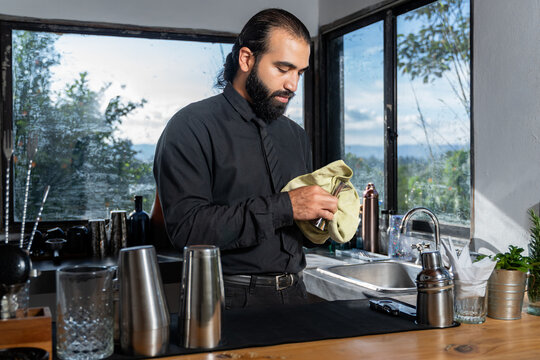 Colombian bartender drying jigger in hotel bar with countryside view and mint.