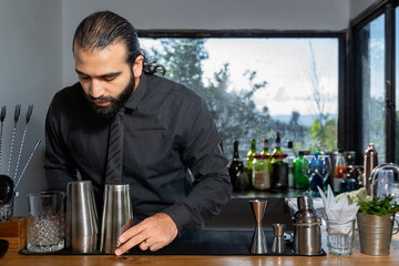Bartender arranging cocktail shakers before starting work in hotel bar with countryside view.