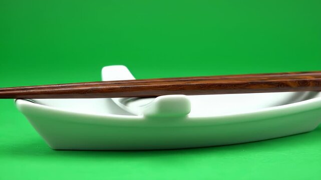 Chopsticks resting on a white bowl against green background.