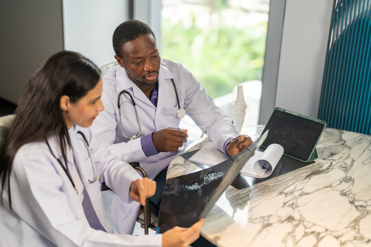 Diverse medical team african male doctor and female doctor collaborating and reviewing medical documents writing and discussing patient data in hospital office, teamwork in healthcare, patient care