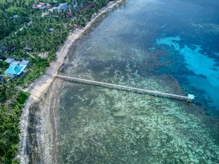 Aerial of long pier over shallow turquoise reef to small hut
