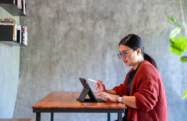 A woman working on a digital tablet with a stylus in a calm workspace. She focuses on creative tasks at a wooden desk, showing modern technology use and remote work lifestyle.