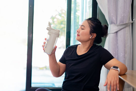 Woman resting after workout at home holding a shaker bottle, enjoying hydration and recovery, representing healthy lifestyle, fitness routine, exercise motivation, and modern wellness. healthcare