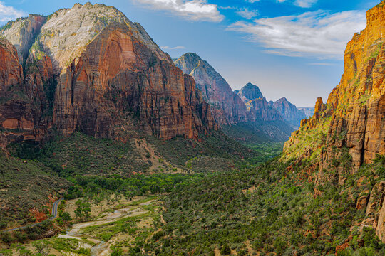 A sweeping canyon panorama reveals towering cliffs, rugged rock formations, and green valley vegetation in Zion National Park. - Powered by Adobe