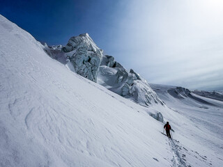 Backcountry skier in bright gear moving across deep snow near dramatic glacier formations in the high Swiss Alps on a clear winter day.