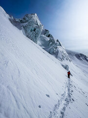 Backcountry skier in bright gear moving across deep snow near dramatic glacier formations in the high Swiss Alps on a clear winter day.