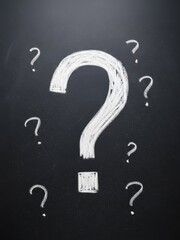 Bold white chalk question mark drawn on a textured dark blackboard, surrounded by smaller question marks, symbolizing conceptual uncertainty, dilemma, and problem-solving strategy.