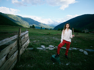 Woman stands with a shovel beside a wooden fence in a rural valley, mountains in the distance, open...