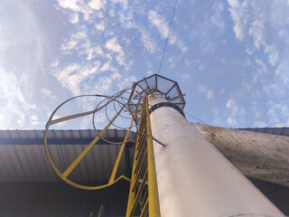 Perspective shot of a tall yellow safety ladder attached to a weathered metal pipe, reaching toward...
