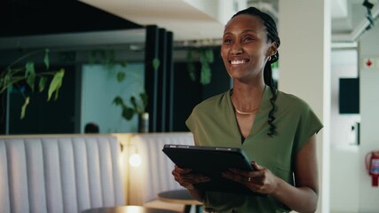 A smiling young black businesswoman with digital tablet walking in office lobby - Powered by Adobe