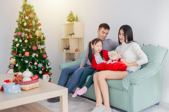 Happy Asian family with daughter celebrating Christmas at home. Parents and child in festive red outfits sitting at table with holiday decorations. Joyful family bonding moment during festive season. - Powered by Adobe