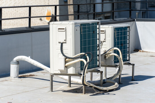 Two modern air conditioning units are professionally installed on a flat building rooftop under bright sunlight for efficient climate control and energy management.