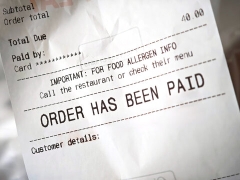 Restaurant receipt closeup detail with &ldquo;order has been paid&rdquo; text and allergen info, takeaway delivery bill on thermal paper showing total due, card payment confirmation, printed checkout slip, nobody