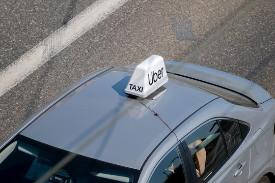 Uber taxi car roof top sign on a silver vehicle driving on an asphalt road, high angle top view from above. Ride sharing app service, urban city transportation business concept, cab symbol, from above